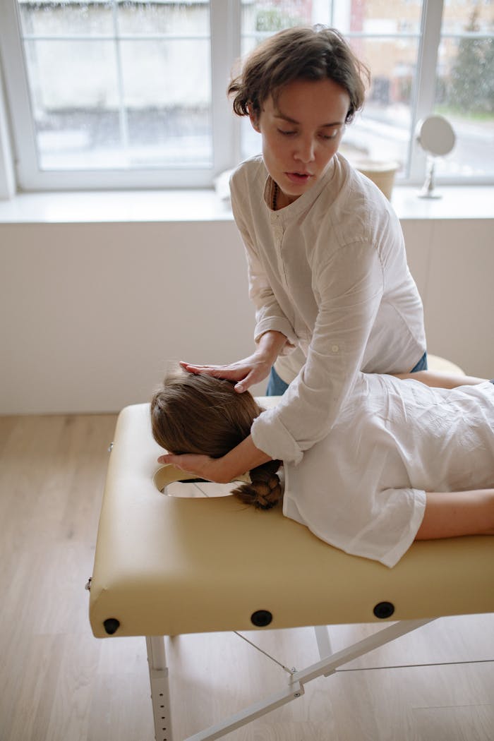 service-01 Massage therapist performing head massage on client on table in a serene indoor setting.